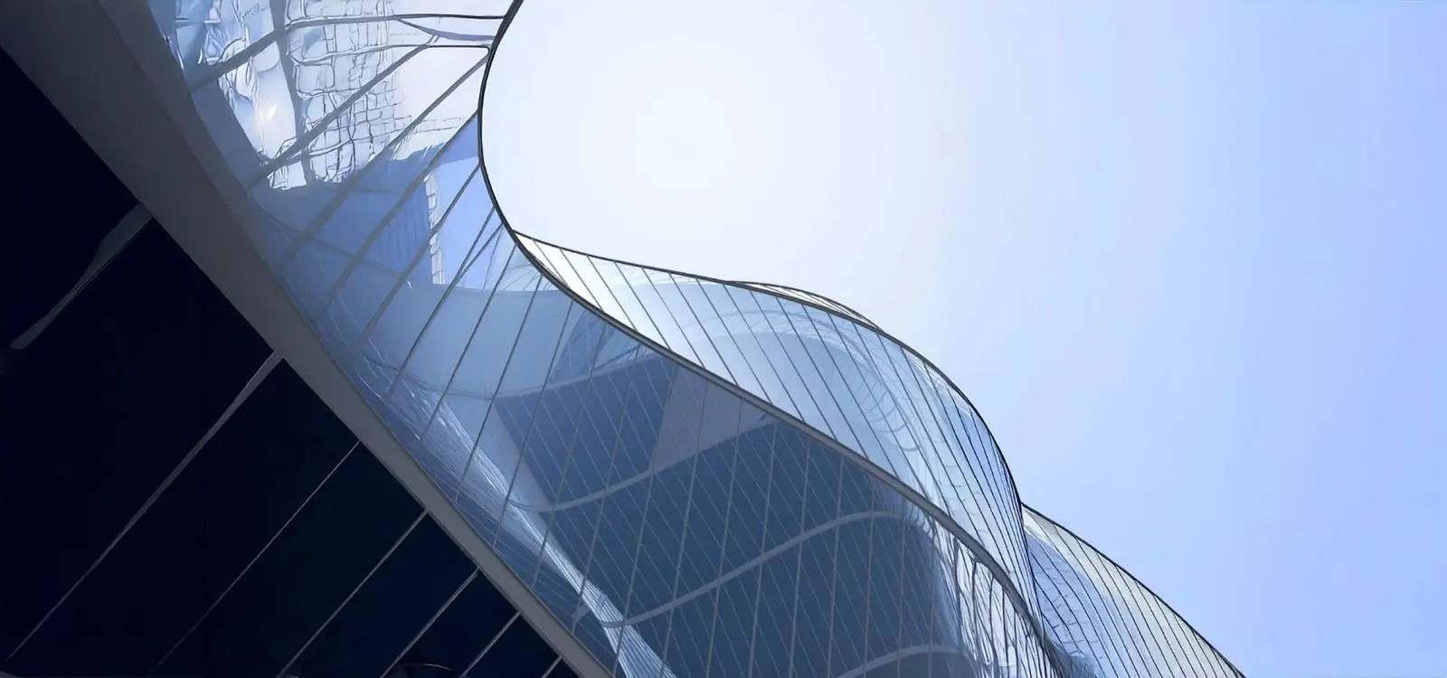 Curved glass facade of a modern architectural structure against a clear blue sky.